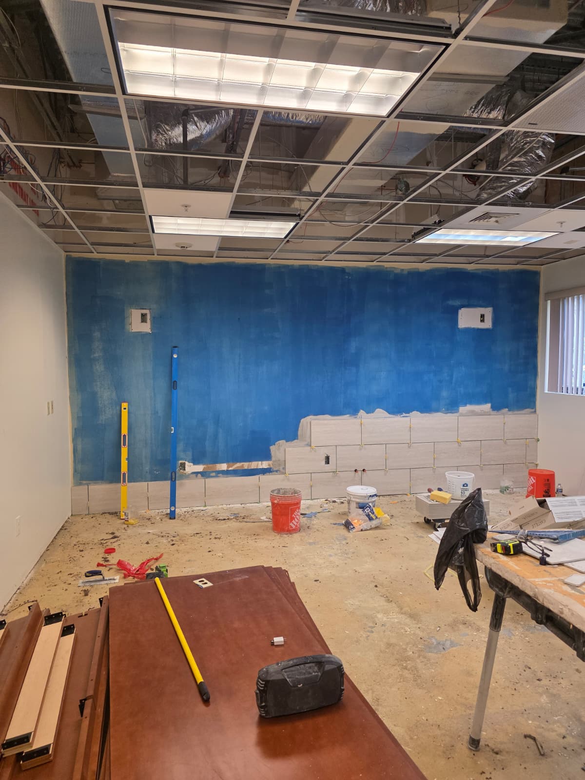 Renovation room with ceiling tiles and wall finishes removed while the ceiling grid and remaining surfaces stay in place