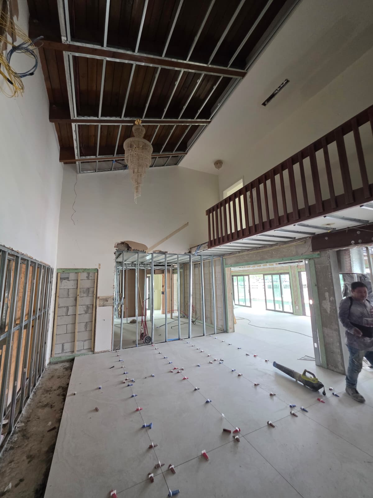 Double-height interior renovation with exposed ceiling framing, retained mezzanine railing, and new flooring work