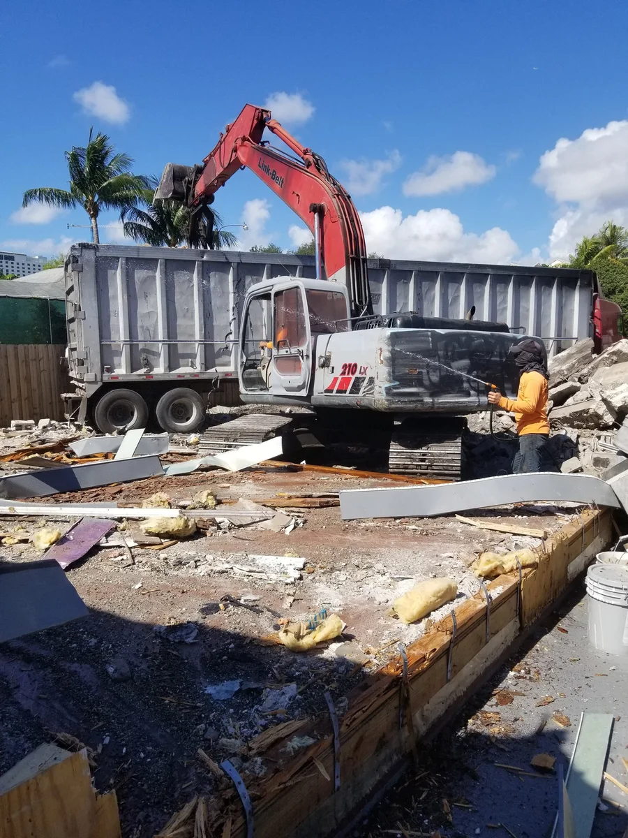 Excavator alongside a dump truck removing debris from a demolition site