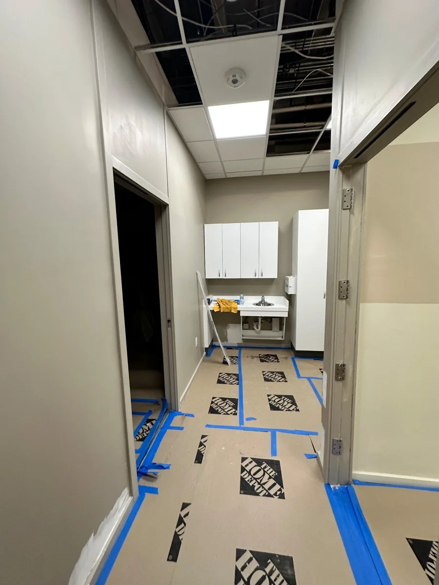 Interior corridor with taped floor protection and opened ceiling panels during renovation